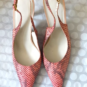 Może przedstawiać: Para butów na obcasie L.K. Bennett z paskiem na pięcie. Buty mają spiczasty nosek i wzór wężowej skóry w odcieniach różu i czerwieni. Obcasy mają małą złotą klamrę i jasnoróżowe wnętrze.