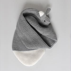 May include: Gray and white knitted scarf with a gray rabbit head on one end. The rabbit has white ears and black eyes.