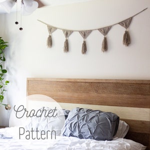 May include: A crochet banner with tassels hangs above a bed with a wooden headboard. The banner is made of beige yarn and has a geometric pattern. The text "Crochet Pattern" is superimposed on the image.