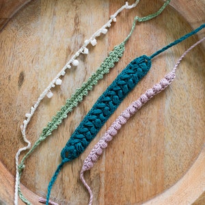 May include: Four crocheted bracelets in different colors and styles, including a teal braided bracelet, a green crocheted bracelet, a pink crocheted bracelet, and a white crocheted bracelet with white beads.