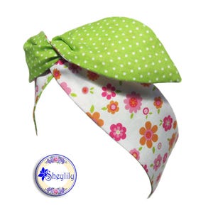 May include: A green and white headband with a polka dot pattern on one side and a floral pattern on the other side. The headband is tied in a knot at the top.
