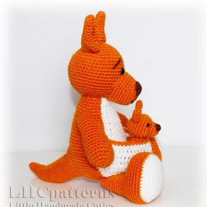 May include: A crocheted orange kangaroo holding a smaller crocheted orange joey in its pouch. The kangaroo has a white pouch and brown eyes. The joey has brown eyes and a white pouch.
