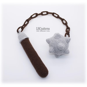 Puede incluir: Juguete de maza medieval tejido a ganchillo con mango marrón, cabeza gris y cadena marrón. El mango tiene una parte superior gris. La cabeza tiene forma de estrella gris. El texto "LHCpatterns Little Handmade Cuties" es visible.