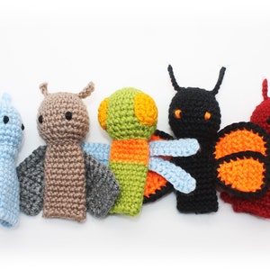 May include: Five crocheted finger puppets shaped like insects. The puppets are blue, brown, green, black, and red. Each puppet has a different design and color scheme.