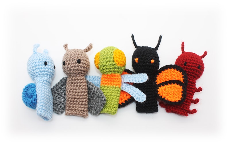 May include: Five crocheted finger puppets shaped like insects. The puppets are blue, brown, green, black, and red. Each puppet has a different design and color scheme.