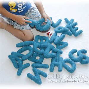 May include: A set of blue crocheted alphabet letters. The letters are arranged on a white surface. The letters are soft and cuddly, perfect for a child's playroom.