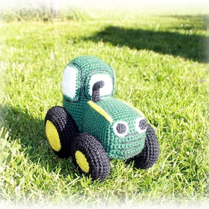 May include: A green crocheted toy tractor with black wheels and yellow rims. The tractor has a white face with black eyes and a black exhaust pipe.
