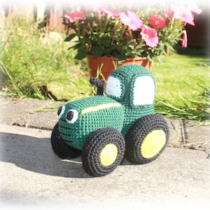 May include: A green crocheted toy tractor with black wheels and yellow accents. The tractor has a white windscreen and black details.