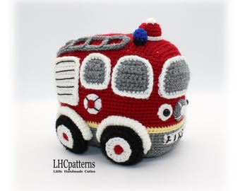 May include: A red, gray, and white crocheted fire truck toy with black wheels and a blue light on top. The truck has a white stripe around the bottom and the word "FIRE" written on the side.