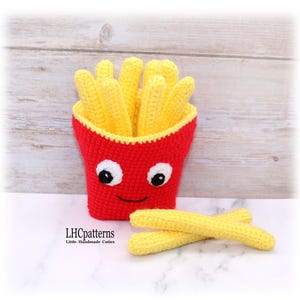Peut inclure: Un récipient rouge crocheté avec un visage souriant, contenant des frites crochetées jaunes. Deux frites supplémentaires sont posées à côté du récipient. Le récipient a des yeux blancs avec des pupilles noires. Le texte "LHCpatterns" est visible.