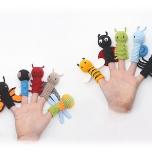 Puede incluir: Un conjunto de ocho marionetas de dedos que representan varios insectos, incluyendo una mariposa, una mariquita, una abeja, una oruga, una libélula y una araña. Las marionnettes están hechas de hilo de crochet en una variedad de colores, incluyendo negro, rojo, amarillo, verde, azul y naranja.