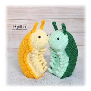 May include: Two handmade crochet caterpillar toys. One is yellow and orange, the other is green and light green. Both have black eyes and are positioned close together. The text "LHCpatterns Little Handmade Cuties" is in the upper left corner.