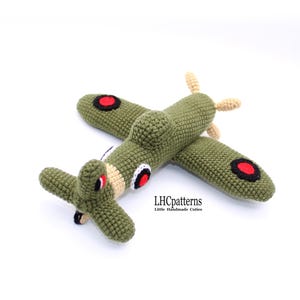 May include: Green crocheted airplane toy with red and black circles on the wings. The toy has a beige propeller and tail. The text "LHCpatterns Little Handmade Cutes" is on the bottom of the toy.