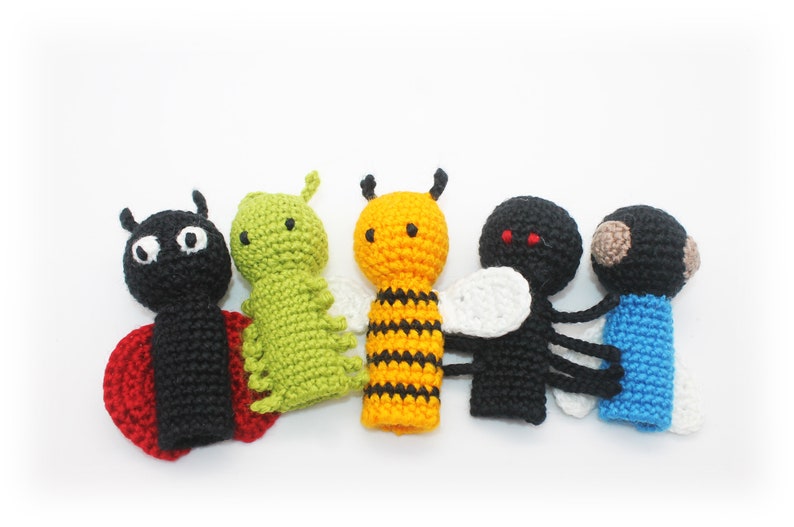 May include: Five crocheted finger puppets shaped like insects. The puppets are a ladybug, a caterpillar, a bee, a fly, and a blue bug. The puppets are all made with different colored yarn.