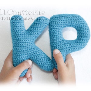 May include: Two crocheted letters, K and P, in a light blue color. The letters are held by two hands.
