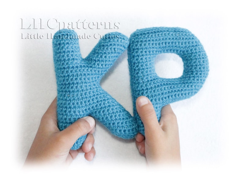 May include: Two crocheted letters, K and P, in a light blue color. The letters are held by two hands.
