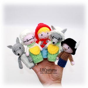Peut inclure: Un ensemble de cinq marionnettes à doigts représentant des personnages du conte de fées Le Petit Chaperon Rouge. Les marionnettes sont crochetées et comprennent le Petit Chaperon Rouge, la grand-mère, le loup et deux autres loups. Les marionnettes sont sur une main, avec le texte "LHCpatterns Little Handmade Cuties" en dessous.