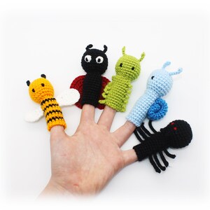 May include: Five finger puppets depicting different insects: a bee, a ladybug, a caterpillar, a snail, and a spider. The puppets are made of crocheted yarn in various colors, including yellow, black, red, green, blue, and white.