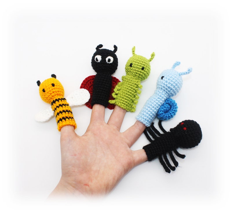 May include: Five finger puppets depicting different insects: a bee, a ladybug, a caterpillar, a snail, and a spider. The puppets are made of crocheted yarn in various colors, including yellow, black, red, green, blue, and white.