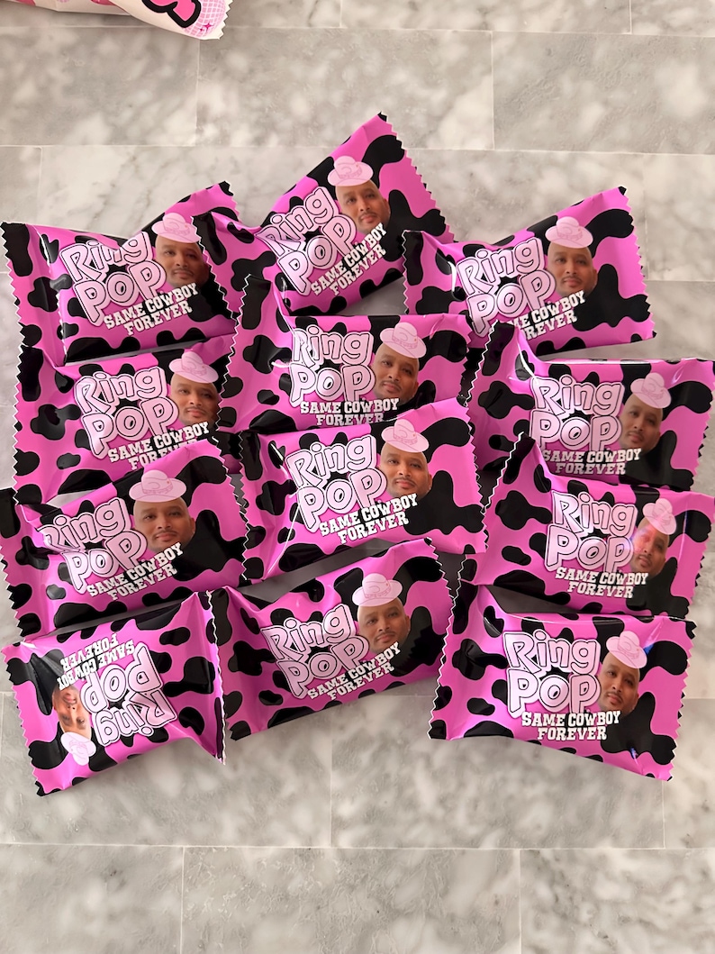 May include: A collection of Ring Pop candy wrappers featuring a pink and black cow print pattern. Each wrapper displays the text Ring Pop and Same Cowboy Forever, along with a photographic portrait of a person wearing a pink cowboy hat.