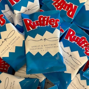 May include: A collection of blue and white Ruffles potato chip bags. The bags feature the Ruffles logo in red and the text "ASHLEY & MATTHEW TOGETHER 9-6-25". The bags are a wedding favor.