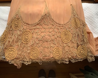 May include: A vintage, peach-colored garment with a delicate lace trim. The lace features a repeating pattern of small, circular motifs.