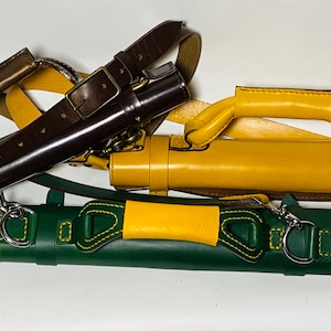 May include: A collection of leather cases in various colors, including dark brown, yellow, and green. Each case has a cylindrical shape with a handle or strap. The cases are designed for carrying items and feature metal hardware.