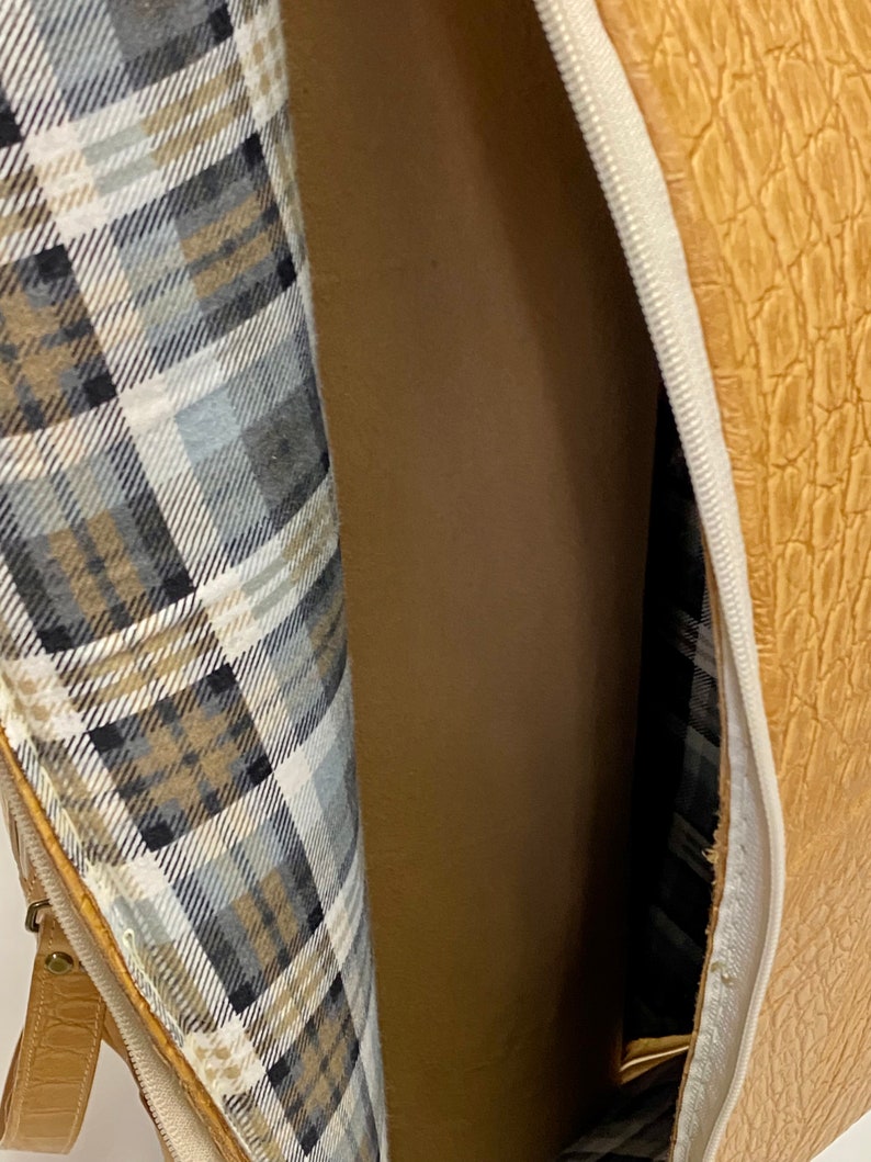 May include: Open view of a tan, textured bag with a zipper. The interior lining features a plaid pattern in shades of gray, white, and tan. The bag's exterior has a reptile-like texture.