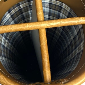 May include: Tan leather golf bag with a plaid interior. The bag has a cross-shaped divider at the top and is stitched with white thread. The interior is a plaid pattern of black, white, and brown.