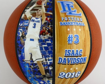 May include: A brown basketball with a blue and white photo of a basketball player on one side and a wood-grain design on the other side. The wood-grain side has the text "Potters Basketball #3 Isaac Davidson 2016".