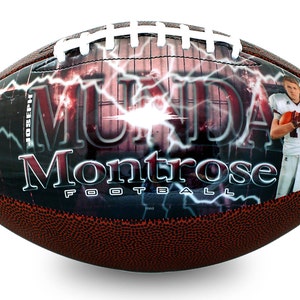 Op de afbeelding: Een bruine en witte voetbal met een zwart en rood ontwerp. Het ontwerp bevat de naam van een speler, "MUNDAY", en de tekst "Montrose Football". Het ontwerp bevat ook een bliksemontwerp en een foto van een speler.