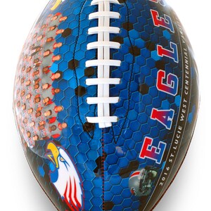 Op de afbeelding: Een blauwe en zwarte voetbal met een wit veterspatroon. De voetbal heeft een zeshoekig patroon en de woorden "EAGLES" en "2016 ST. LUCIE WEST CENTENNIAL VARSITY" erop gedrukt. Er is een rood, wit en blauwe adelaar afbeelding op de voetbal.