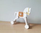 Christmas horse on wheels, white rocking horse retro toy, white horse with brown blanket saddle and a snowflake, decorative Xmas horse