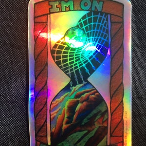 Puede incluir: Una pegatina holográfica con un diseño de reloj de arena colorido. La pegatina dice "I'm on Taos Time" y tiene una fecha de copyright de 2020.