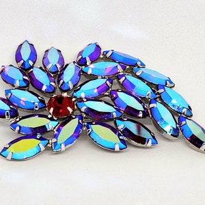 May include: A silver brooch featuring a cluster of iridescent blue marquise-shaped rhinestones with a single red rhinestone at the centre.