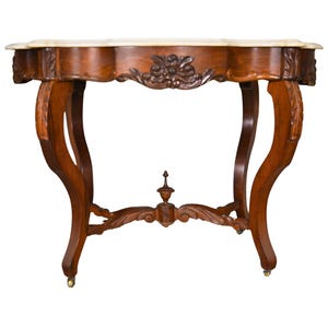 May include: A brown wooden console table featuring a smooth, light-colored stone top with a scalloped edge. The apron and legs are decorated with carved floral motifs. The table stands on four curved legs with small brass casters at the base.