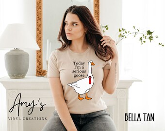 Peut inclure: Un t-shirt beige avec une oie blanche portant une cravate rouge et le texte "Today I'm a serious goose".