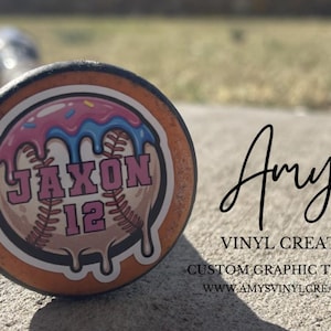May include: A baseball bat end with a custom graphic. The graphic features a baseball with a donut design, the name "Jaxon" and the number "12". The text "Amy's Vinyl Creations" is also visible.