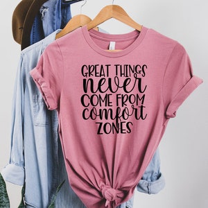 Könnte beinhalten: Ein pinkfarbenes T-Shirt mit dem Aufdruck "Great things never come from comfort zones" in Schwarz.