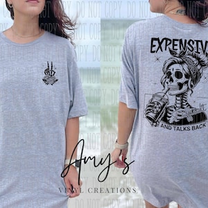 May include: Gray t-shirt with a black graphic of a skeleton with a peace sign and roses on the left side and a skeleton with a coffee cup and the text "Expensive and Talks Back" on the right side.