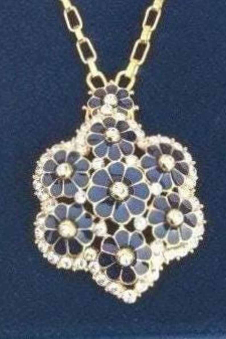 May include: A gold chain necklace with a pendant featuring a cluster of seven black enamel flowers with gold centers and clear crystal accents.