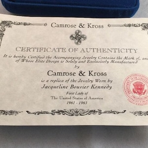 May include: A certificate of authenticity for jewelry, stating that the piece is a replica of the jewelry worn by Jacqueline Bouvier Kennedy, First Lady of the United States of America from 1961 to 1963. The certificate is signed by Camrose & Kross and features a seal of the President of the United States.