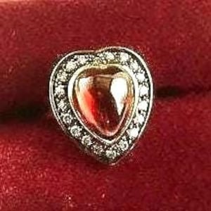 May include: A gold heart-shaped charm with a red gemstone in the center and a border of small clear gemstones.