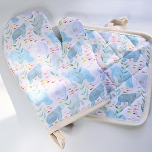 May include: A white oven mitt and pot holder set. The set features a pattern of blue sea cows, green seaweed, and colorful fish. The oven mitt has a loop for hanging. The pot holder is square and quilted.