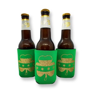 May include: Three green foam beer coolies with a gold glitter shamrock design. Each shamrock has five gold stars in the center.