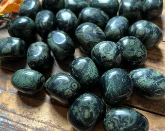 May include: A collection of tumbled green and black serpentine stones. The stones are smooth and polished, with a variety of patterns and swirls.