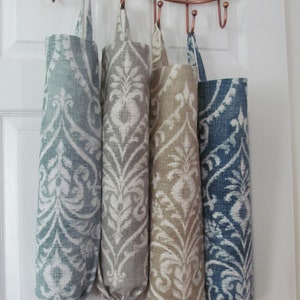 May include: Four fabric bag dispensers in shades of blue, gray, and tan, each with a white floral pattern. The bags hang from a copper-colored rack, offering a decorative and functional storage solution.