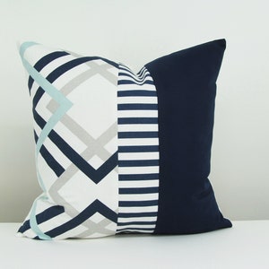 May include: A decorative pillow with a geometric pattern in shades of blue, white, and gray. The pillow has a navy blue backing.