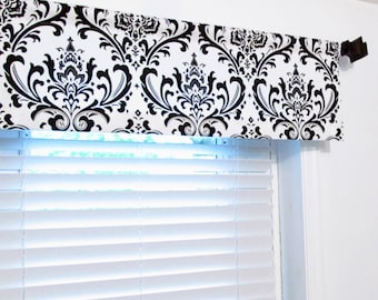 May include: A black and white damask patterned valance with a black metal rod. The valance is hanging above a white window blind.