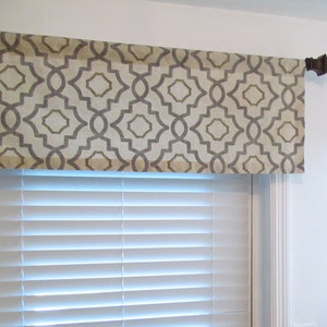 May include: A beige and gray patterned valance with a geometric design. The valance is hung on a brown curtain rod.